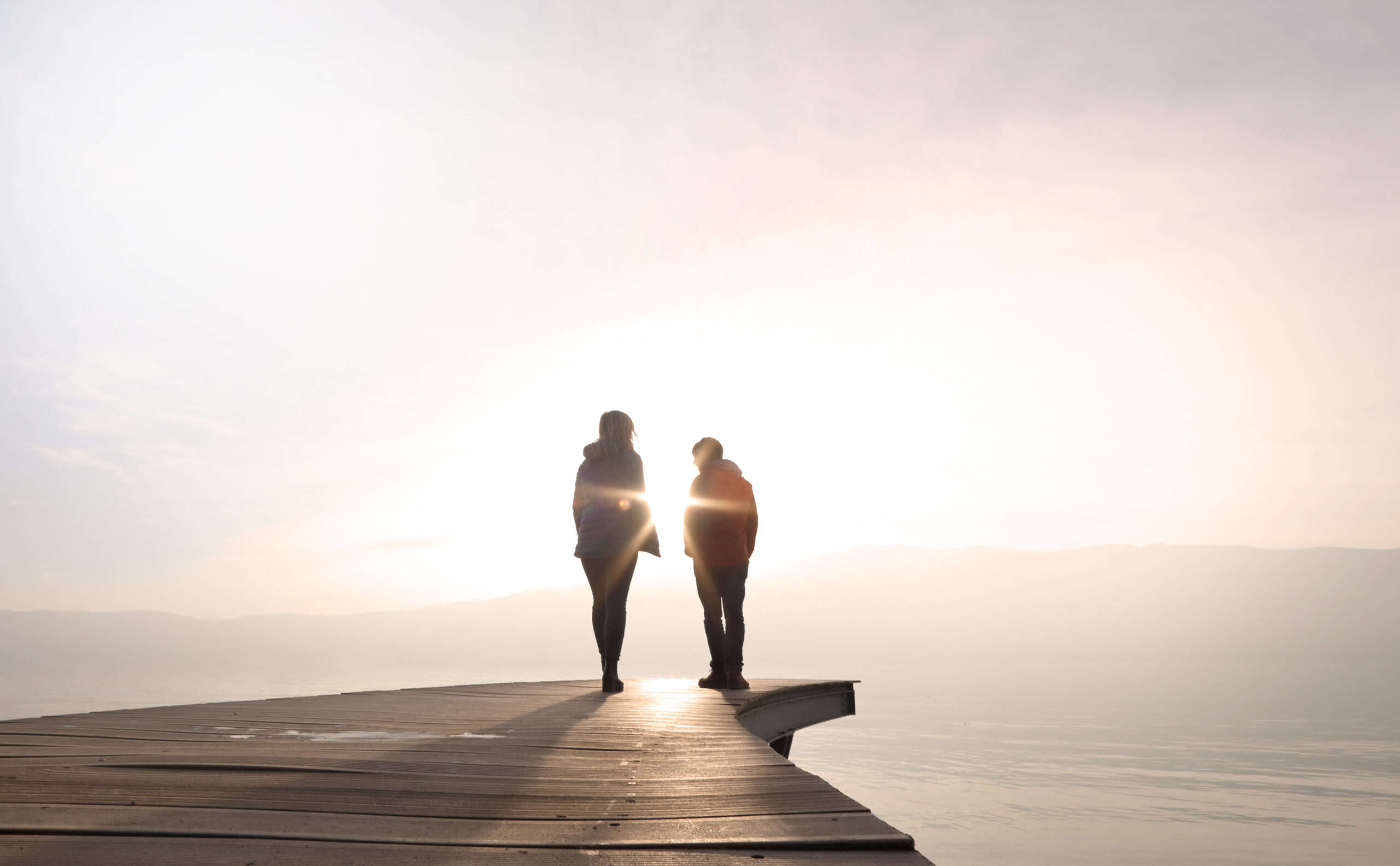 Ein Bild zeigt zwei Menschen mit Herzinsuffizienz, die Hand in Hand auf einem Steg in den Sonnenuntergang gehen. Dies veranschaulicht, wie sie dank DiGA ProHerz sorgenfrei durch den Tag gehen können.